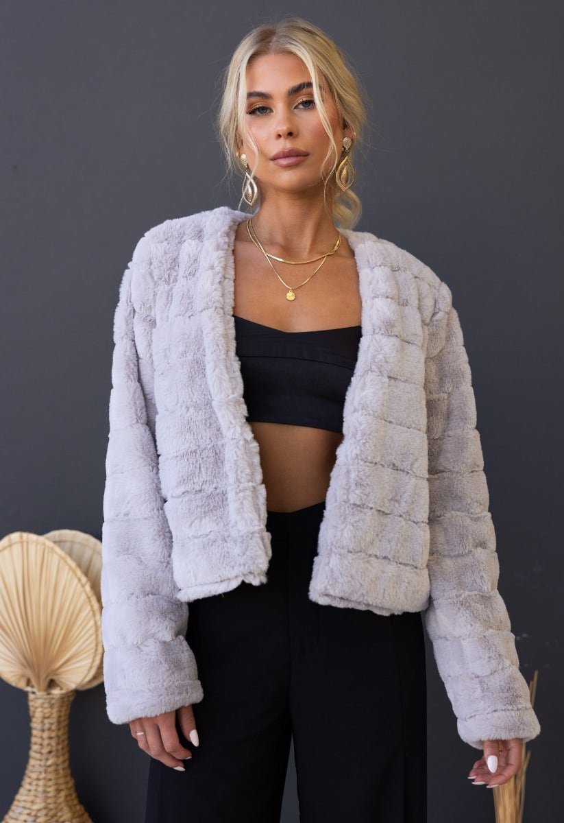 Aviana faux fur jacket in light gray, featuring hook & eye fastening and soft lining, styled with a black crop top.