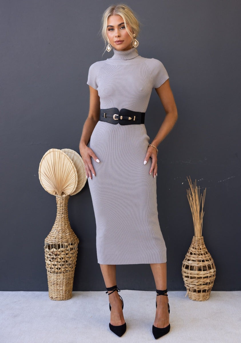 Woman in a ribbed knit Ulina midi dress with turtle neckline and black belt, styled for a chic look.