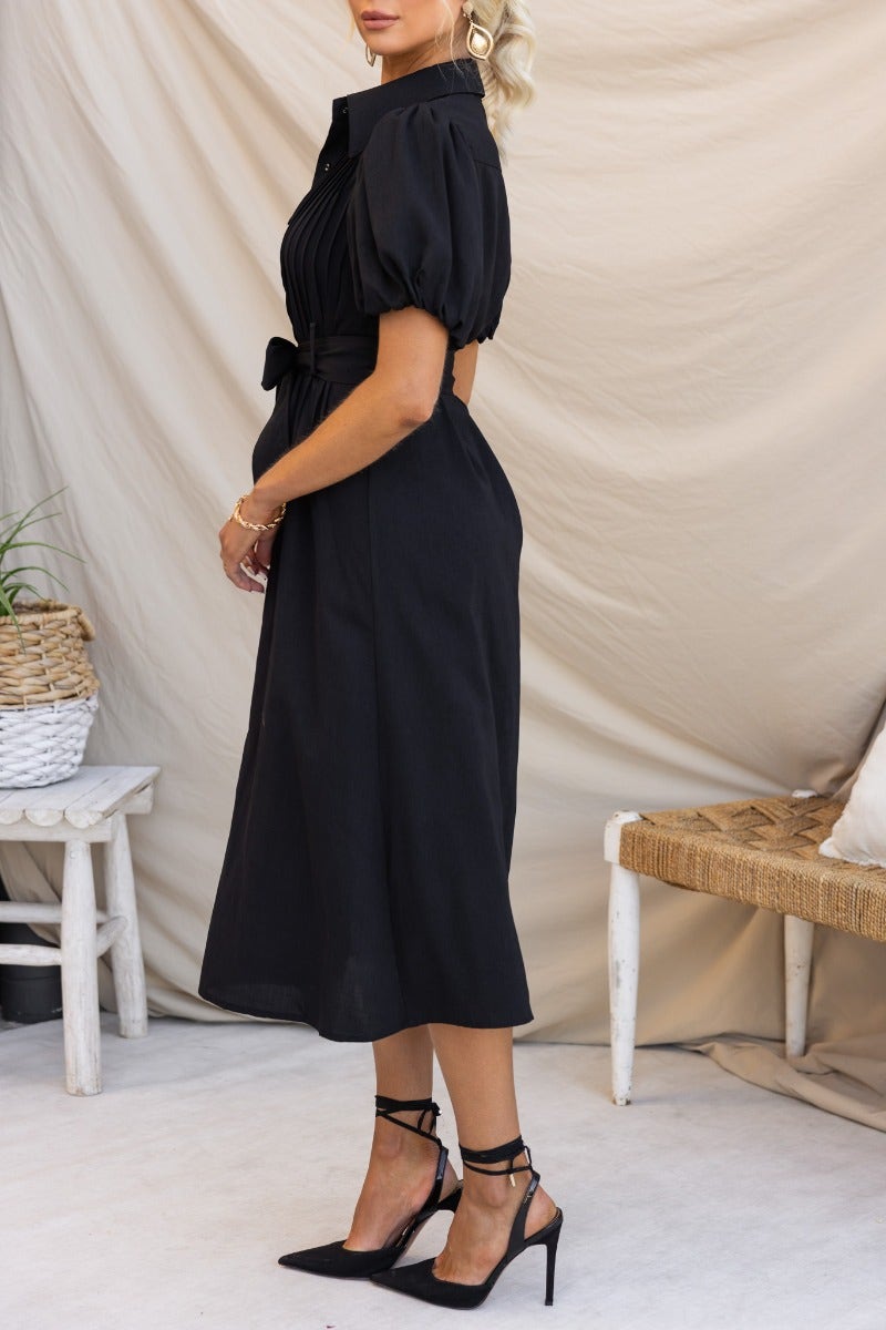 Side view of a stylish black Sorrento Midi Dress featuring a high neckline, button-up front, and removable fabric belt.