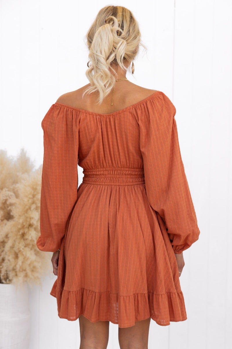 Back view of a rust-colored cotton Getaway Dress with elastic sleeves and a ruffled hemline.