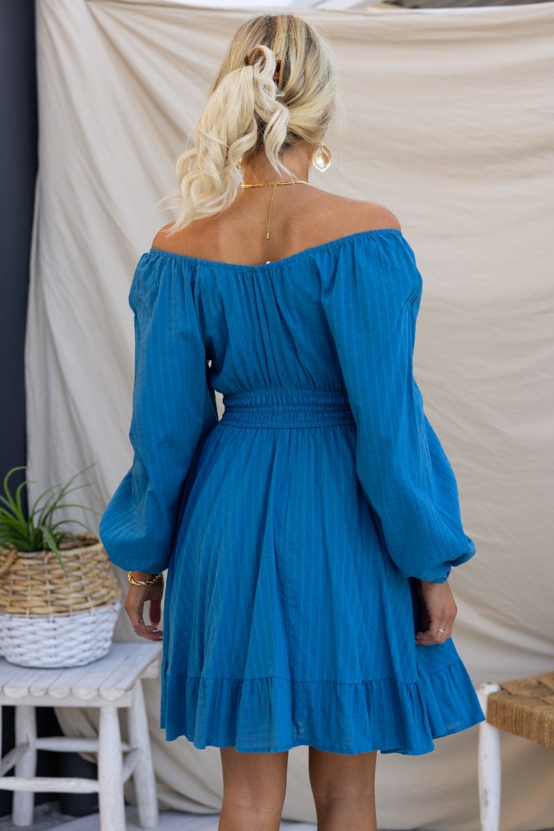 Back view of a blue cotton getaway dress with off-shoulder sleeves and tie detail, showcasing a fitted waist and flared skirt.