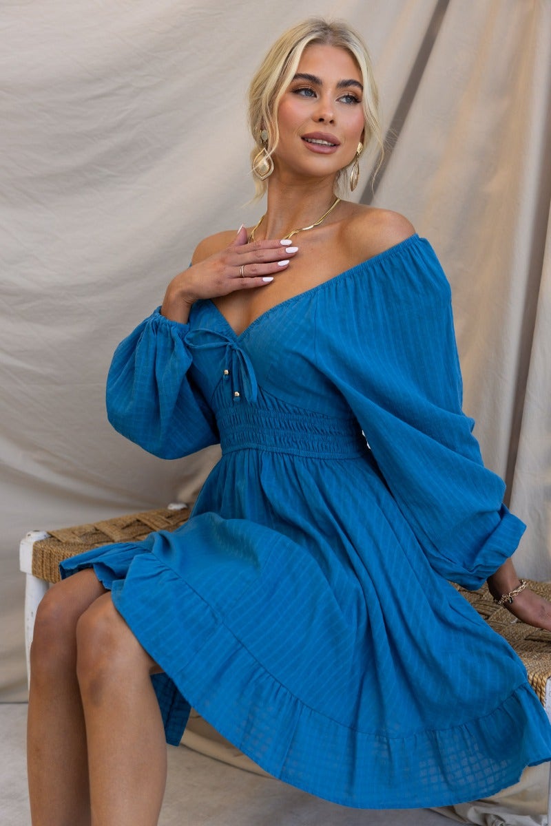 Model wearing a teal getaway dress with puff sleeves, tie neckline, and fitted waist, showcasing a relaxed summer style.