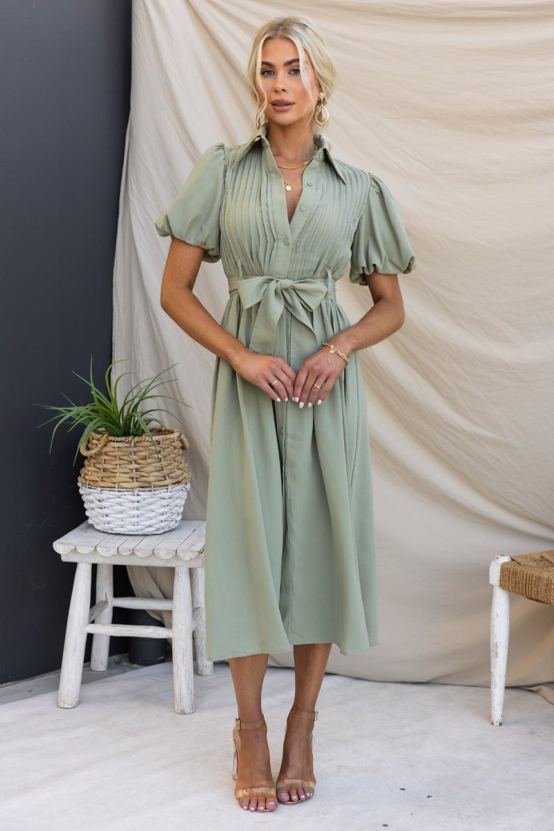 Model wearing a sage green Sorrento Midi Dress with high neckline, collar, button-up front, and removable belt.