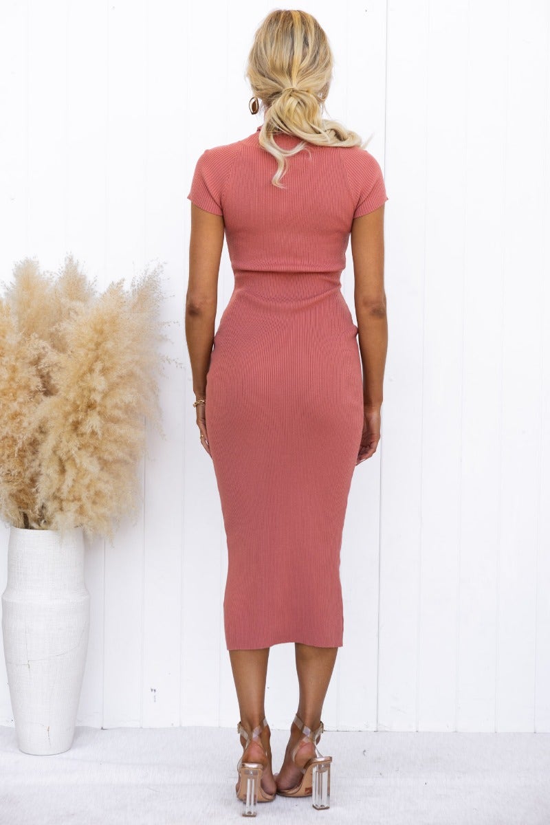 Back view of a model in a ribbed knit Ulina Midi Dress with a turtle neckline in a coral shade, styled with strappy heels.