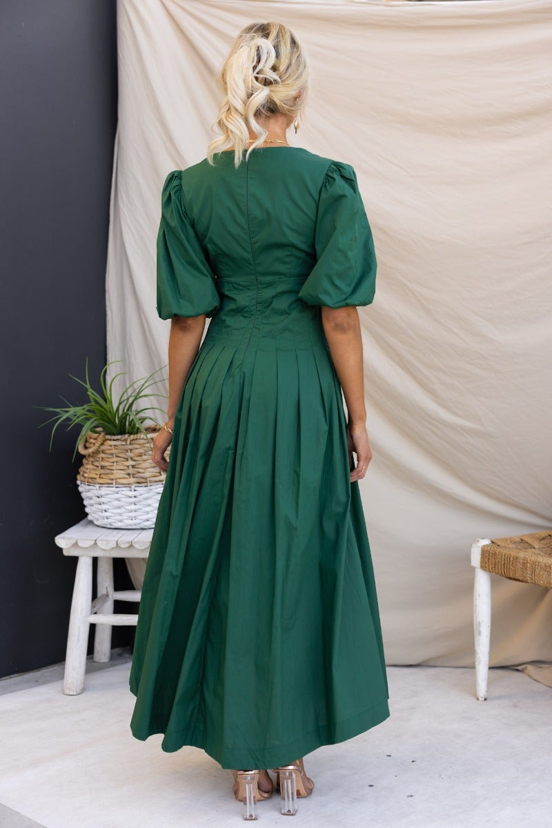 Back view of a green Maloney Maxi Dress with puff sleeves and pleat details, styled in a bright setting.