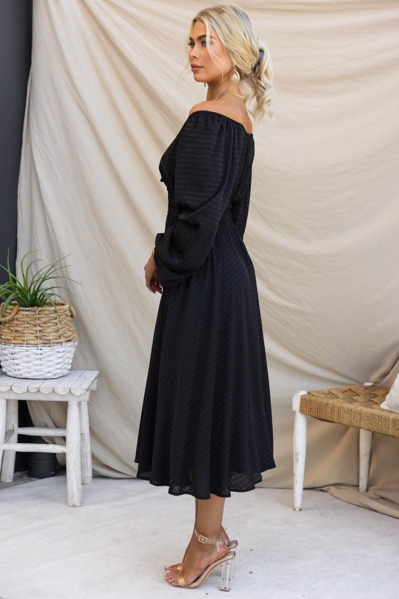 Black textured midi dress with elastic fittings and tie detail, featuring a stylish off-shoulder design and pockets.
