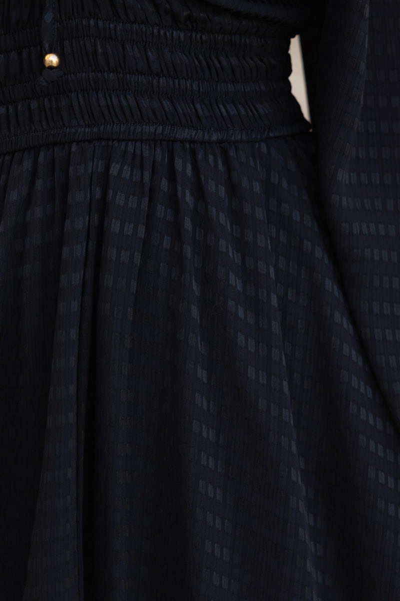 Close-up of black textured midi dress featuring elastic fit and tie detail at neckline.