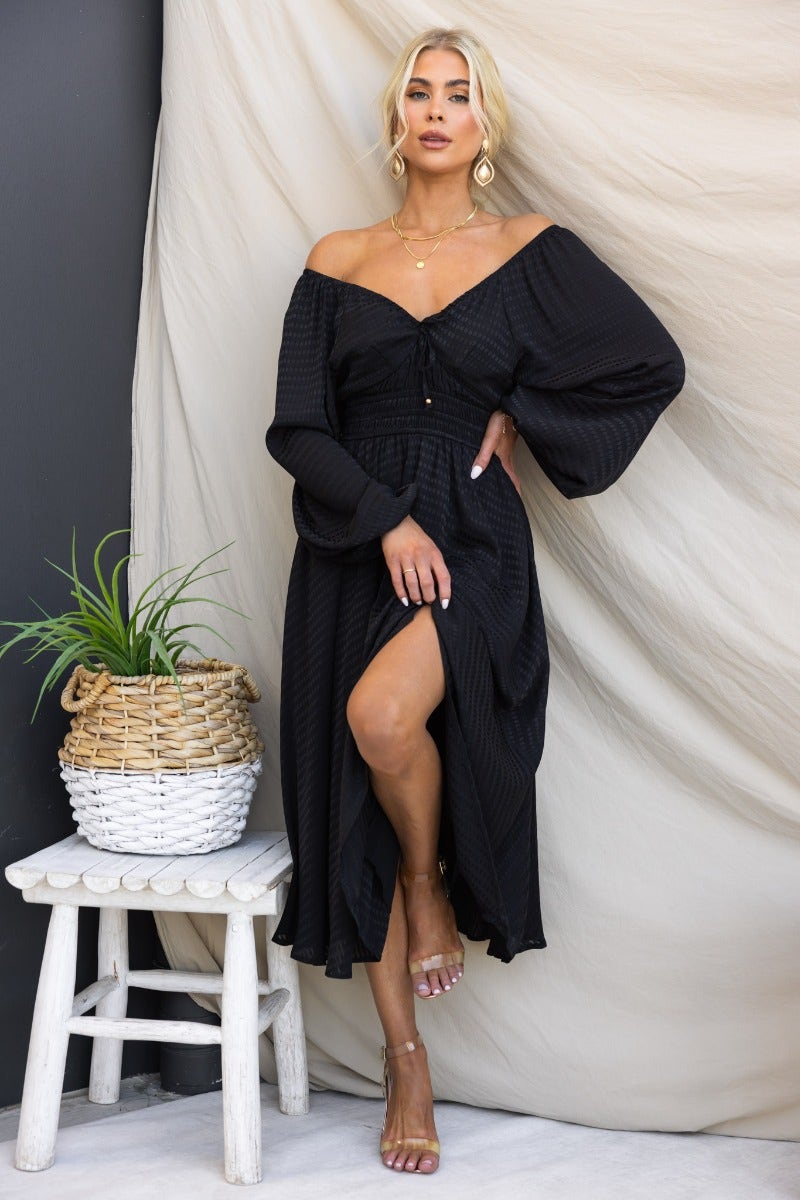 Black textured midi dress featuring elastic sleeves and tie neckline, styled with a side slit and pockets.