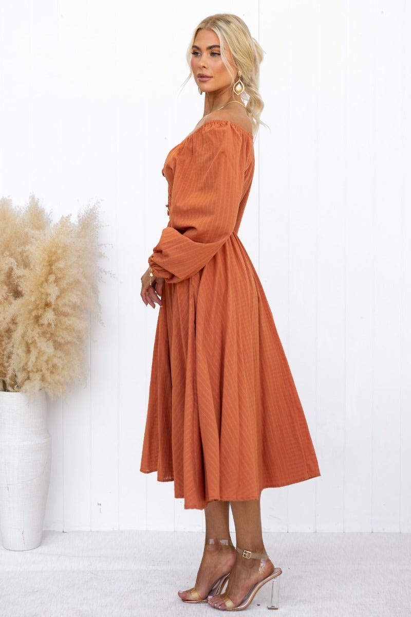 Hemingway Midi Dress in rust color, featuring off-shoulder styling, long sleeves, and a flowing skirt.