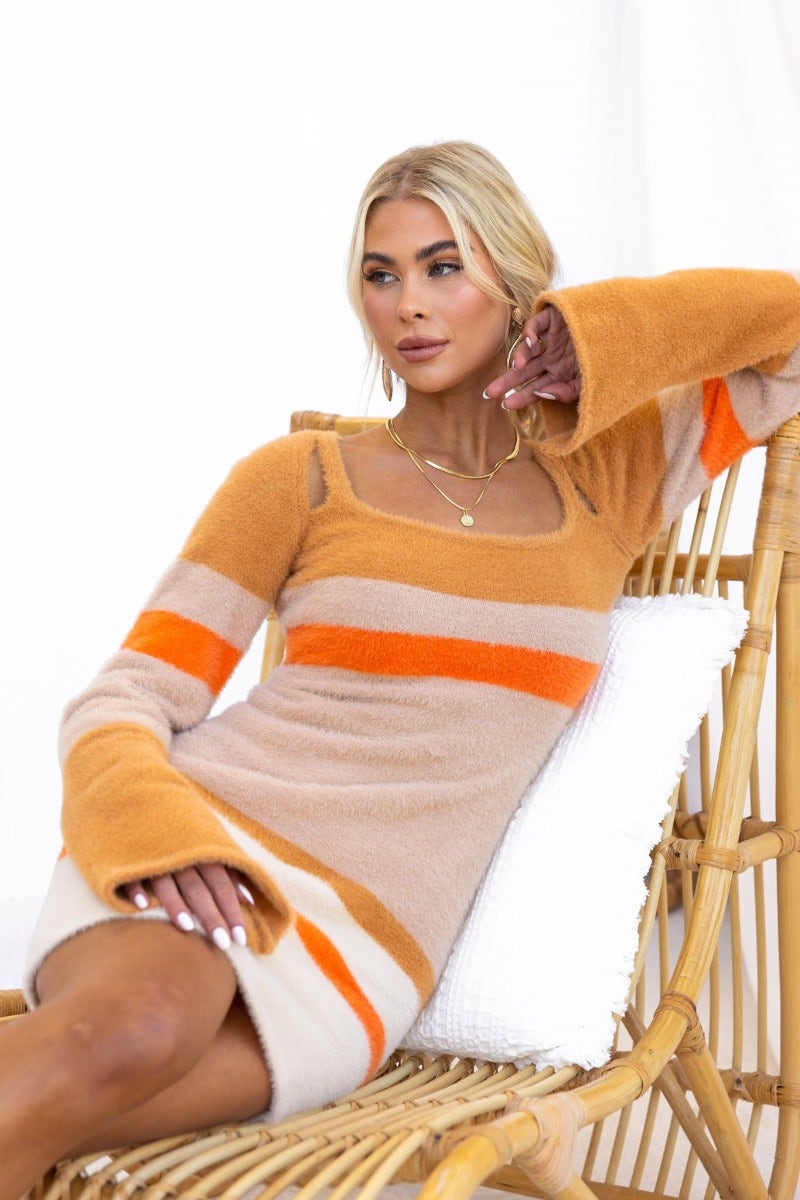 Model in Tynan Dress featuring fluffy knit material, round neckline, and flare sleeves, styled with neutral and orange stripes.