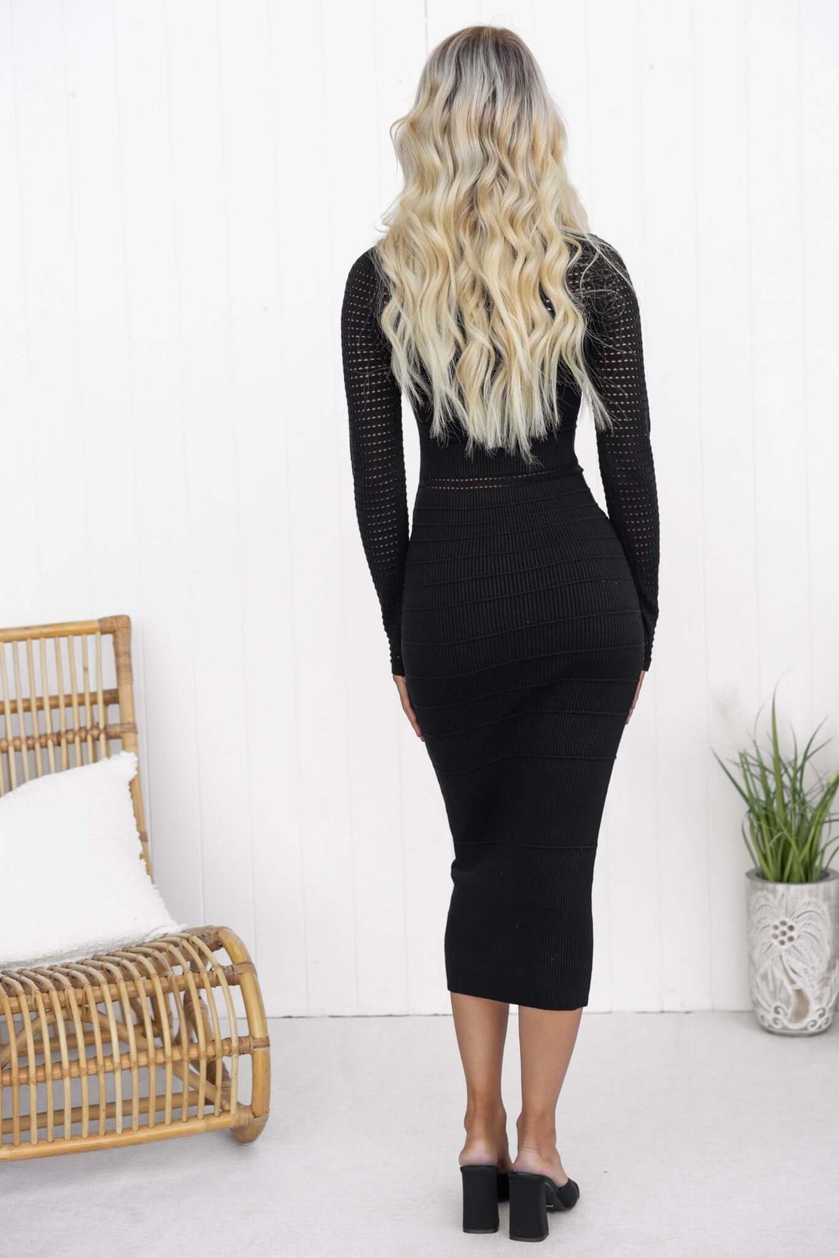 Back view of a woman in a black Kokomo midi dress with open weave knit, styled with wavy blonde hair.