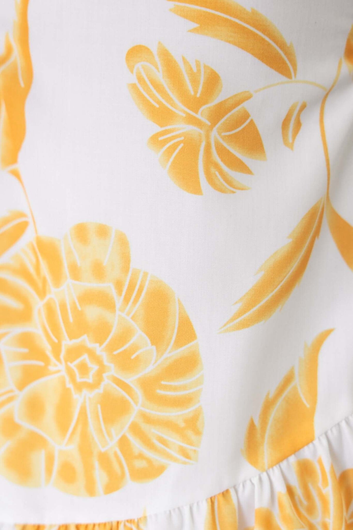 Close-up of the Odessa Maxi Dress featuring a white fabric with vibrant yellow floral patterns, showcasing its stylish design.