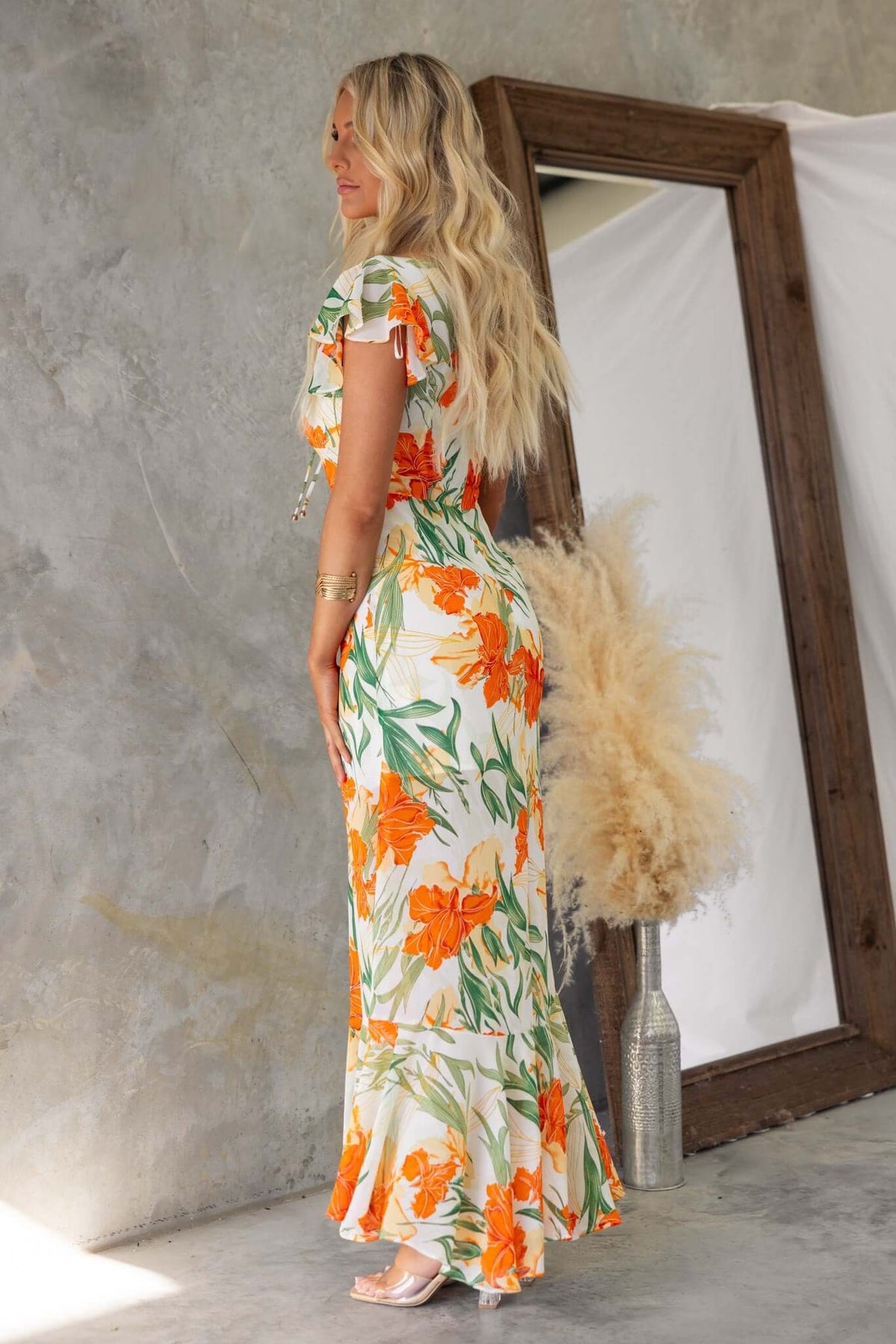 Woman in floral print Tranquil Maxi Dress with ruffles and tie detail, showcasing a stylish summer outfit.