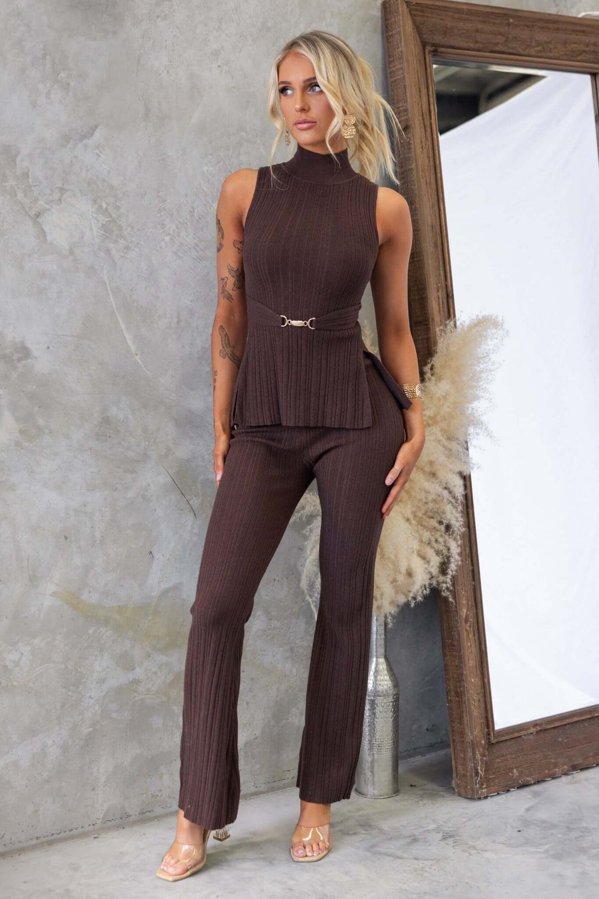 Woman wearing a brown ribbed knit Burling Top with high neckline, gold buckle detail, and stylish splits at the front.