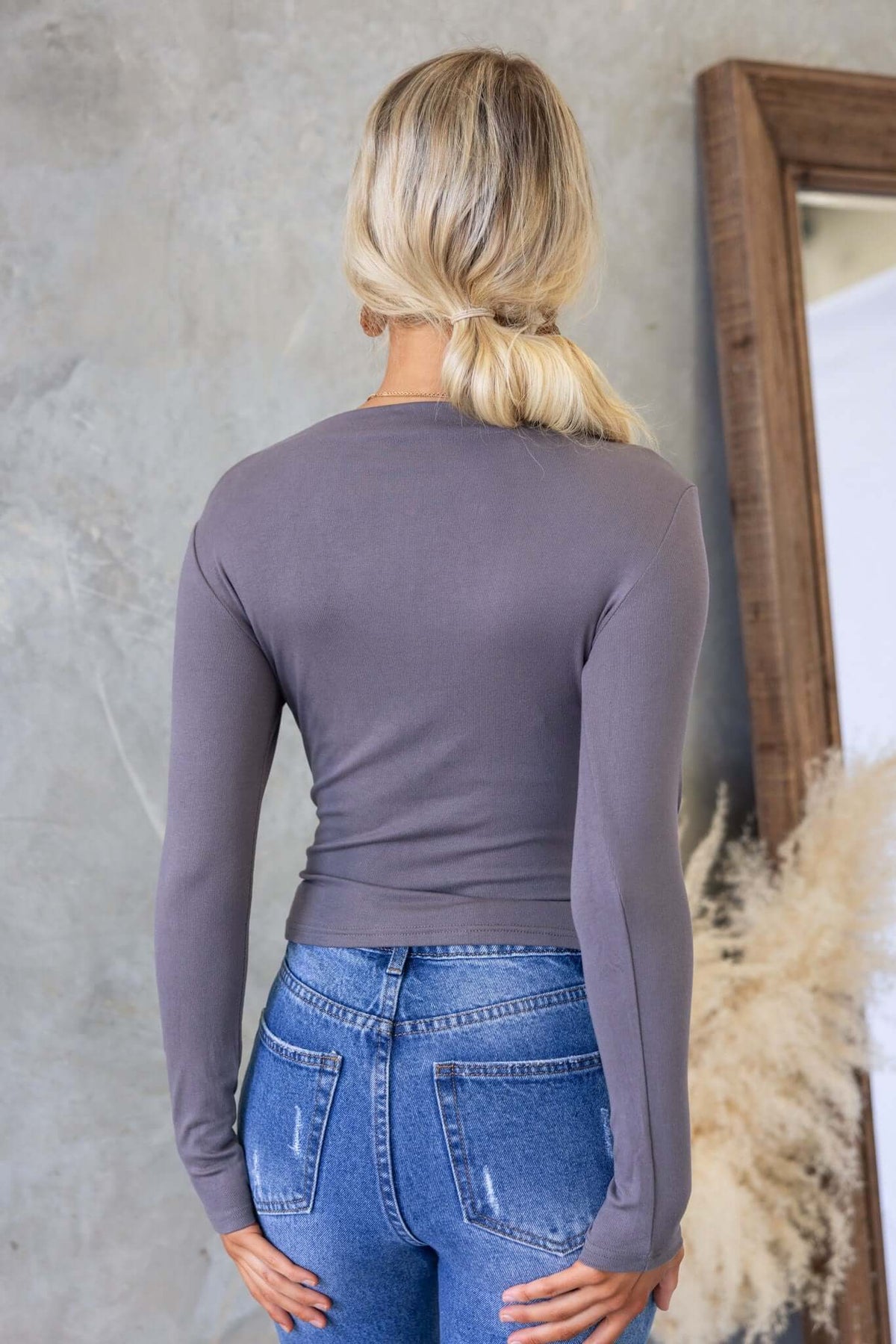 Back view of a woman wearing a gray Iletta Top with long sleeves and fitted style, paired with high-waisted jeans.
