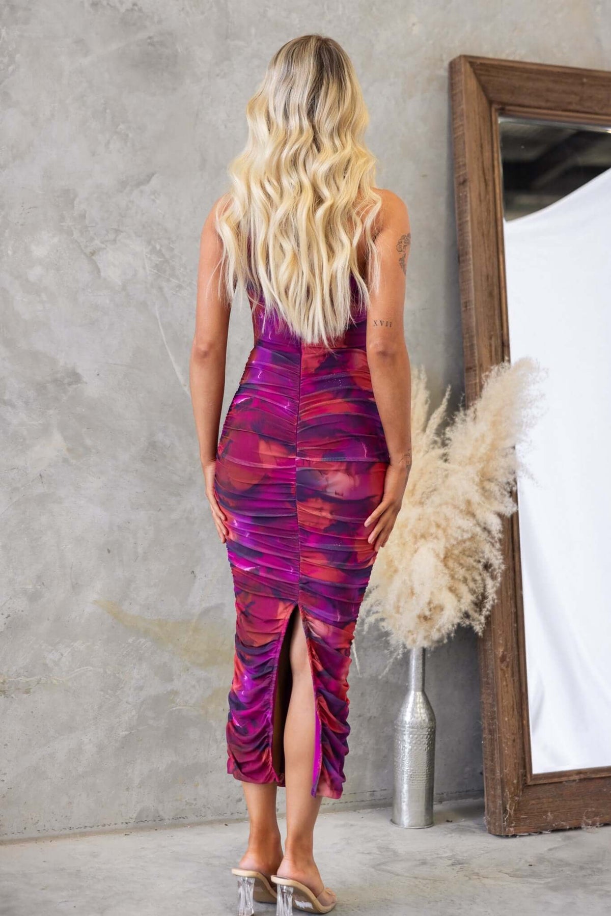 Back view of a model wearing the Stolen Kiss Maxi Dress in vibrant mesh, featuring ruching and a stylish back split.