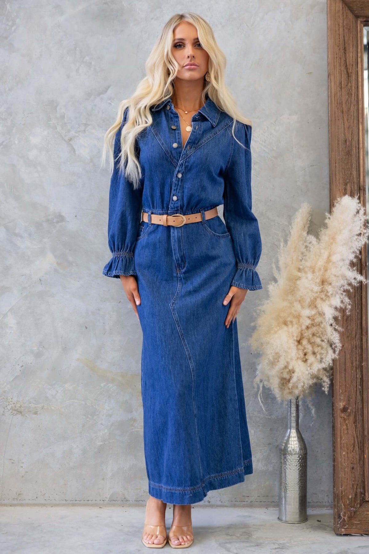 Model wearing Elwood Denim Maxi Dress with a belted waist and puff sleeves against a rustic backdrop.