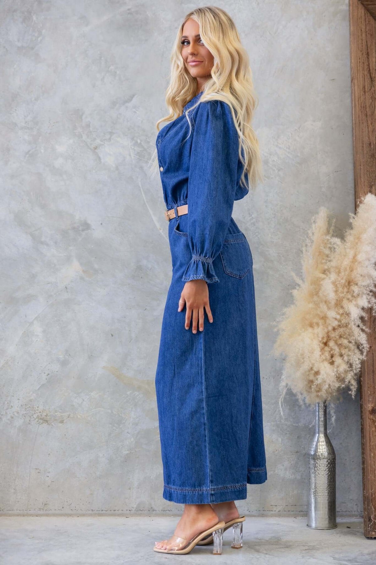 Side view of a woman wearing a denim maxi dress with a collar, button-up front, and elastic waist showcasing a relaxed fit.