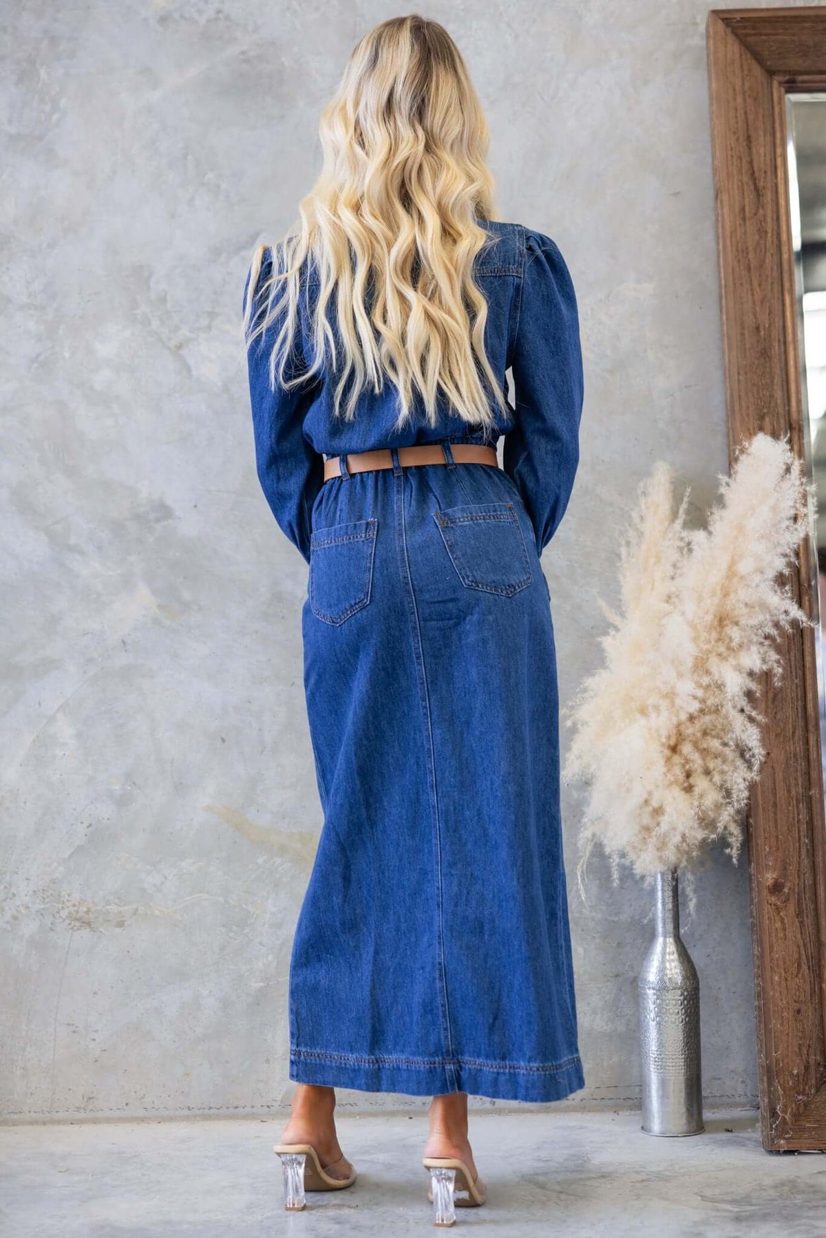 Woman wearing Elwood Denim Maxi Dress with a cinched waist and long sleeves, styled with a belt, showcasing its back view.