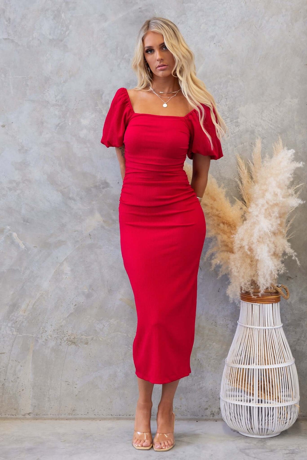 Red Topeka Midi Dress featuring ruched sides, puff sleeves, and a back split styled with a trendy backdrop.