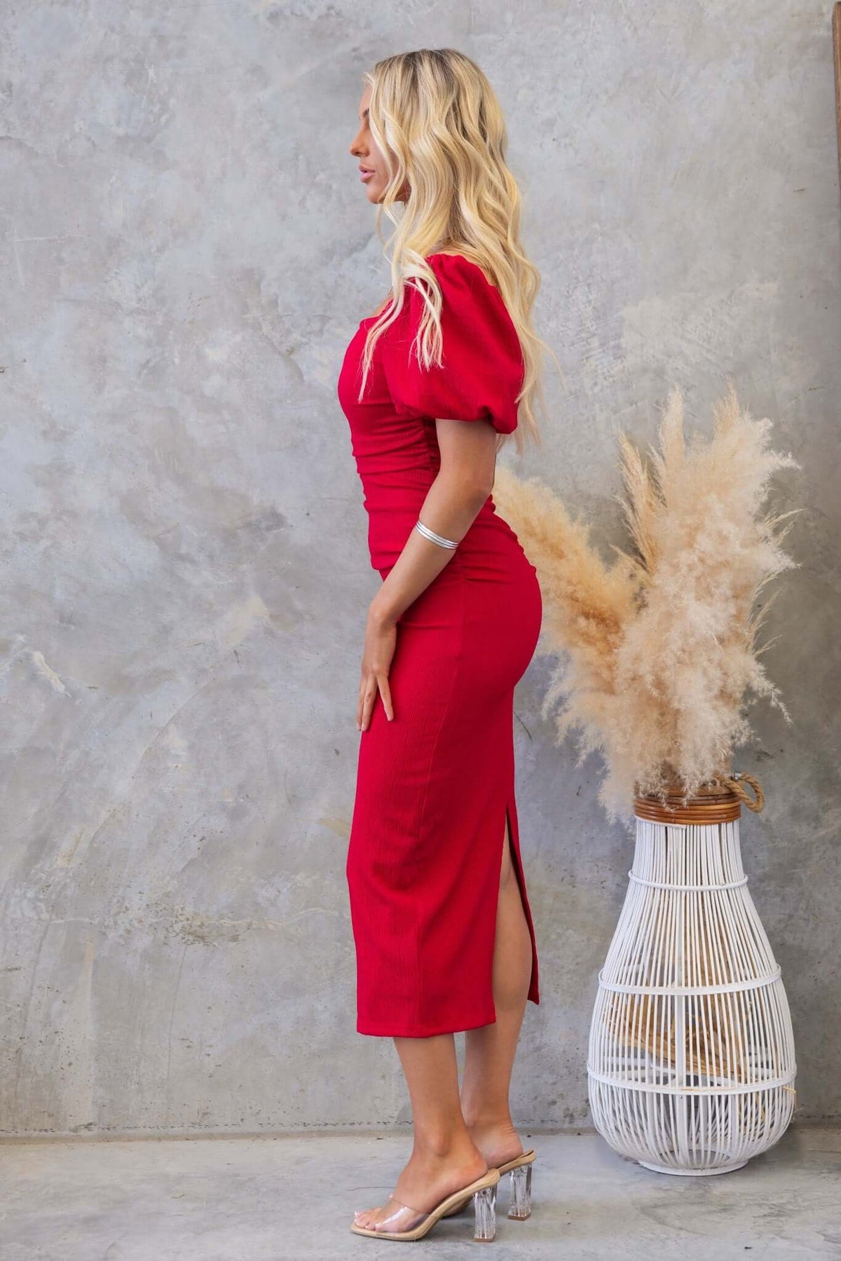 Side view of a woman wearing a red Topeka Midi Dress with puff sleeves, back split, and ruching details.