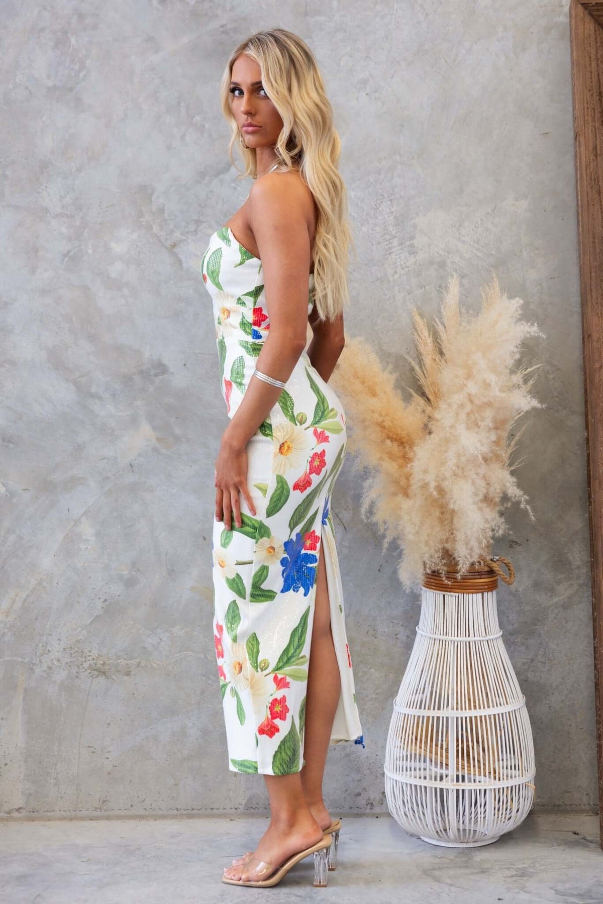 Model wearing a strapless Frutta Maxi Dress with floral print and high split, showcasing a stylish summer look.