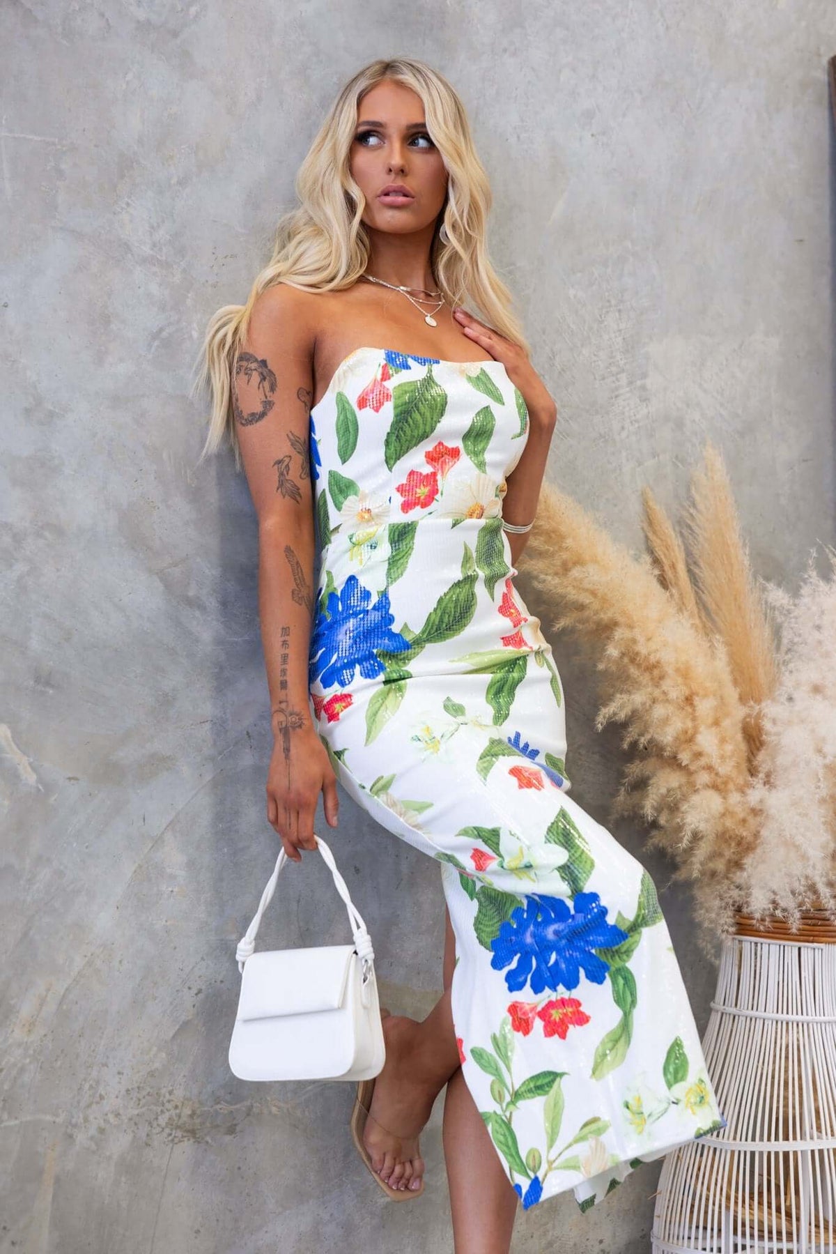 Model wearing Frutta Maxi Dress with floral print, strapless design, and high split, accessorized with a white handbag.