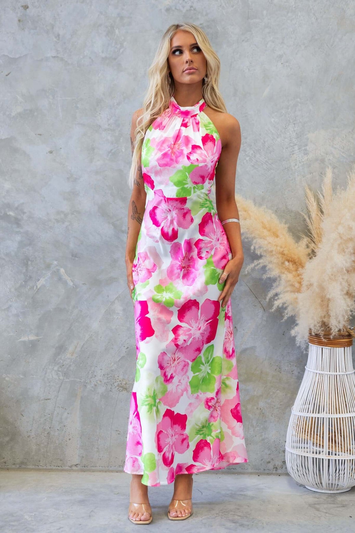 Model wearing the Forbidden Love Maxi Dress with a floral pattern in pink and green, featuring a high tie neckline and satin finish.