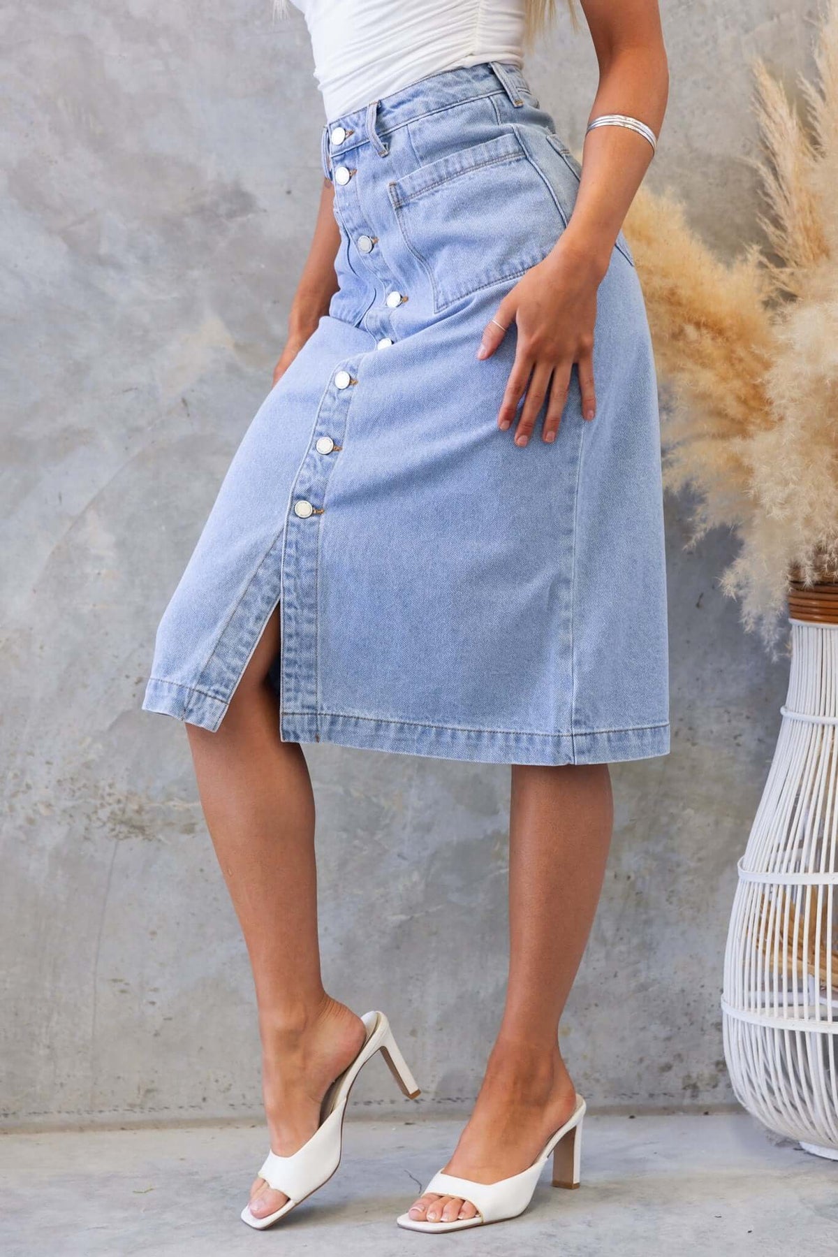 Soma Denim Midi Skirt featuring a button-up front and mid-high waist fit, styled with white heels and a chic outfit.