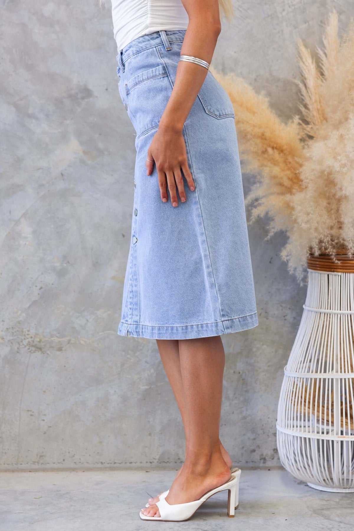 Side view of Soma Denim Midi Skirt in light blue, featuring a high waist, button-up front, perfect for casual styling.