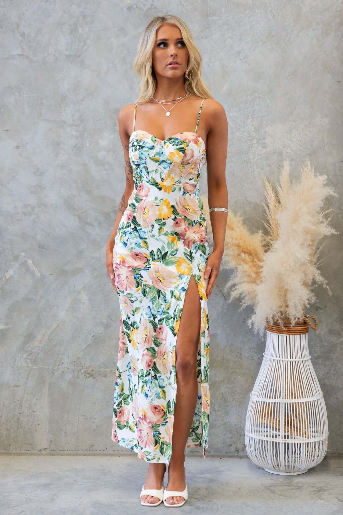 Model wearing the Prato Maxi Dress with floral print, adjustable straps, and a front split, styled with a background of neutral tones.