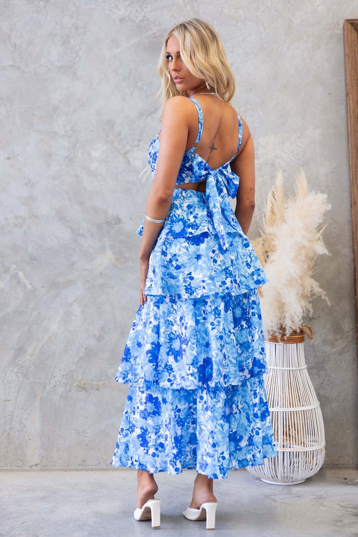 Model wearing blue floral Peyton Maxi Dress with adjustable straps and multi-tier ruffle skirt from the back view.