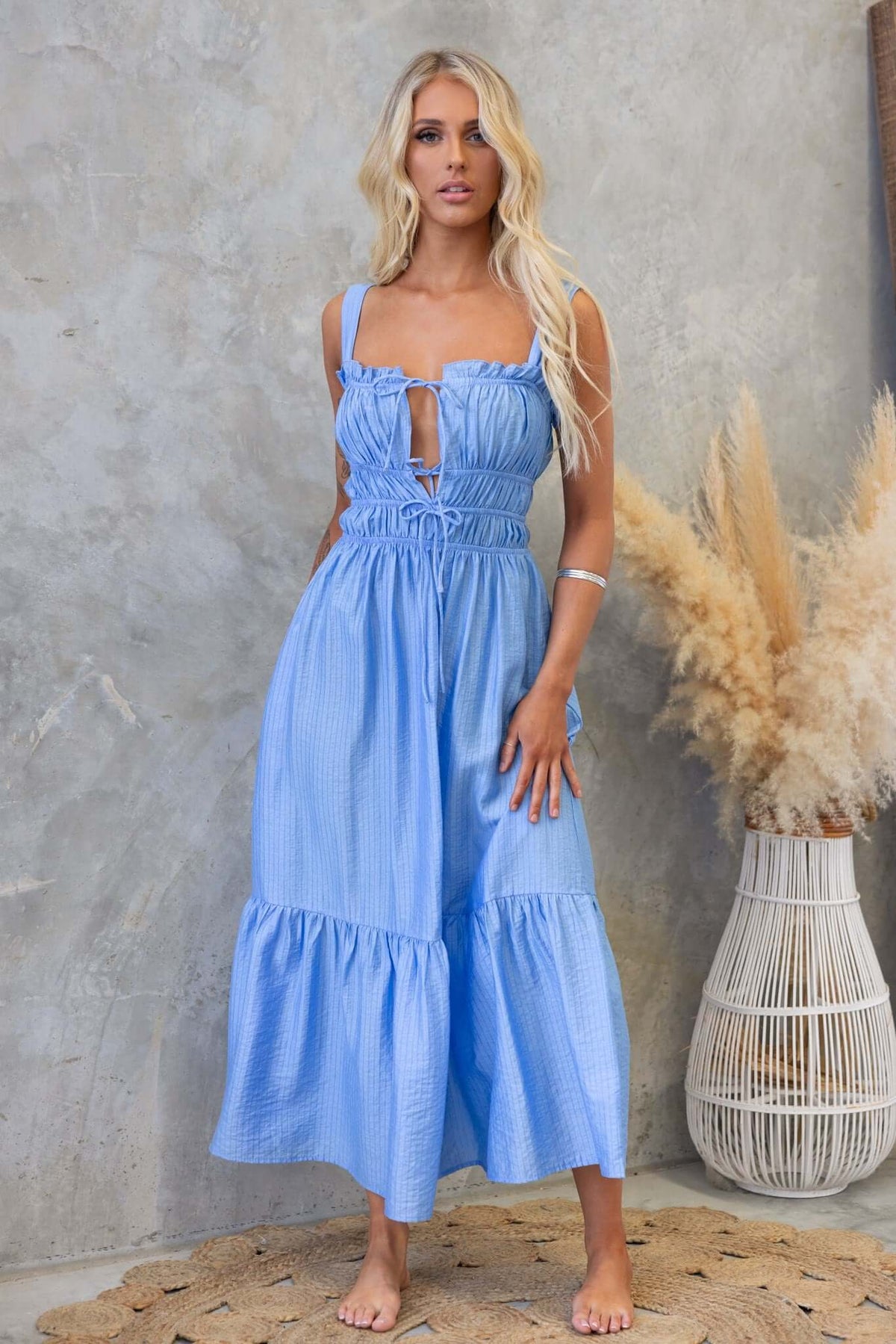 Shanina Midi Dress in blue with tie details at bust, textured fabric, and flowing skirt, styled against a natural backdrop.