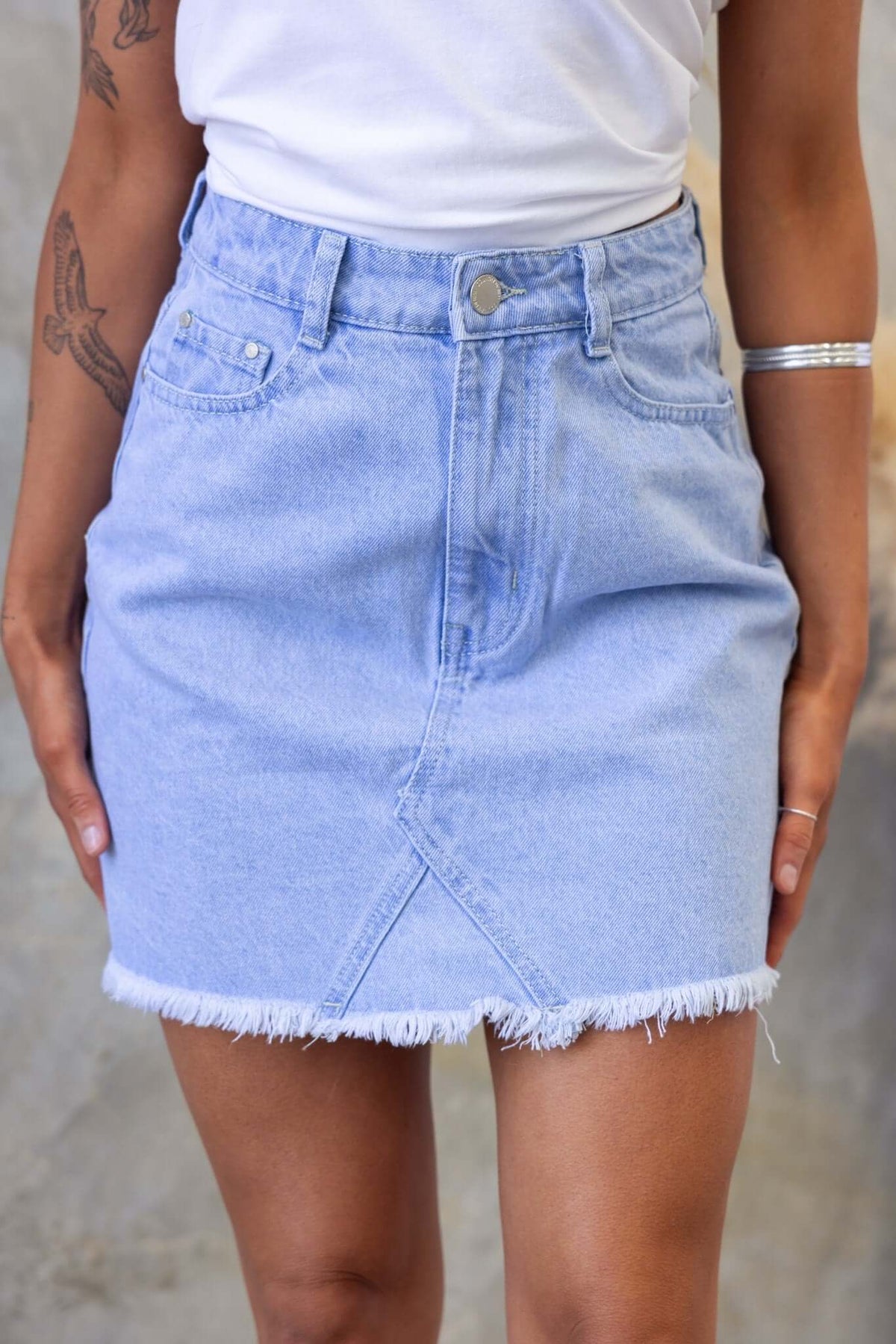 Light blue denim skirt with raw hem, mid-high waist fit, and front pockets, perfect for casual summer outfits.