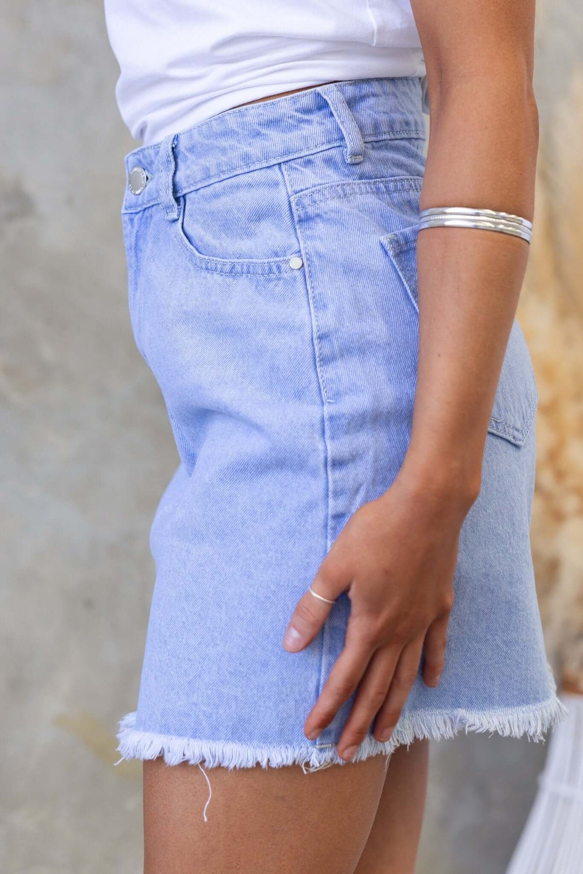 Side view of Orange County Denim Skirt featuring a mid-high waist, pockets, and a raw hem in light blue wash.