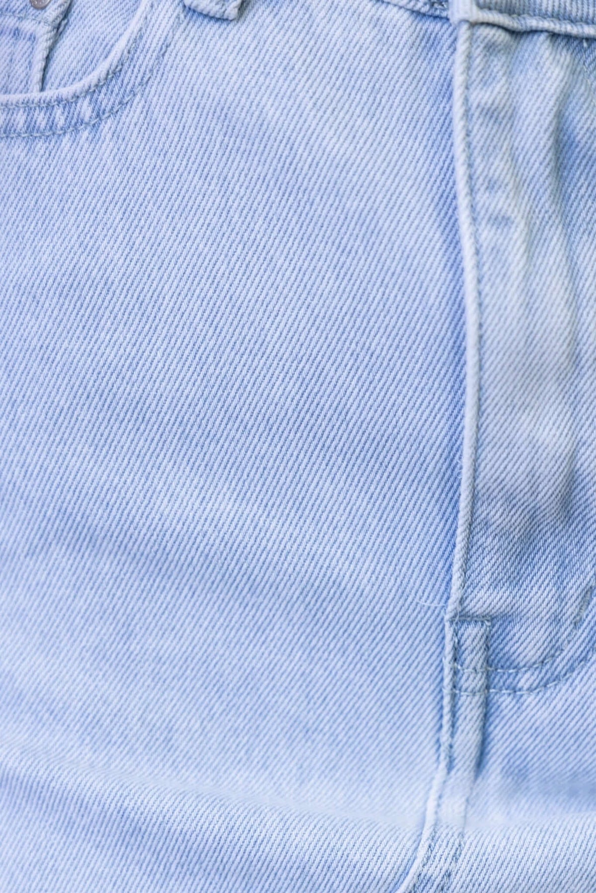 Close-up of light blue denim fabric showing raw hemline and pocket details of an Orange County denim skirt.