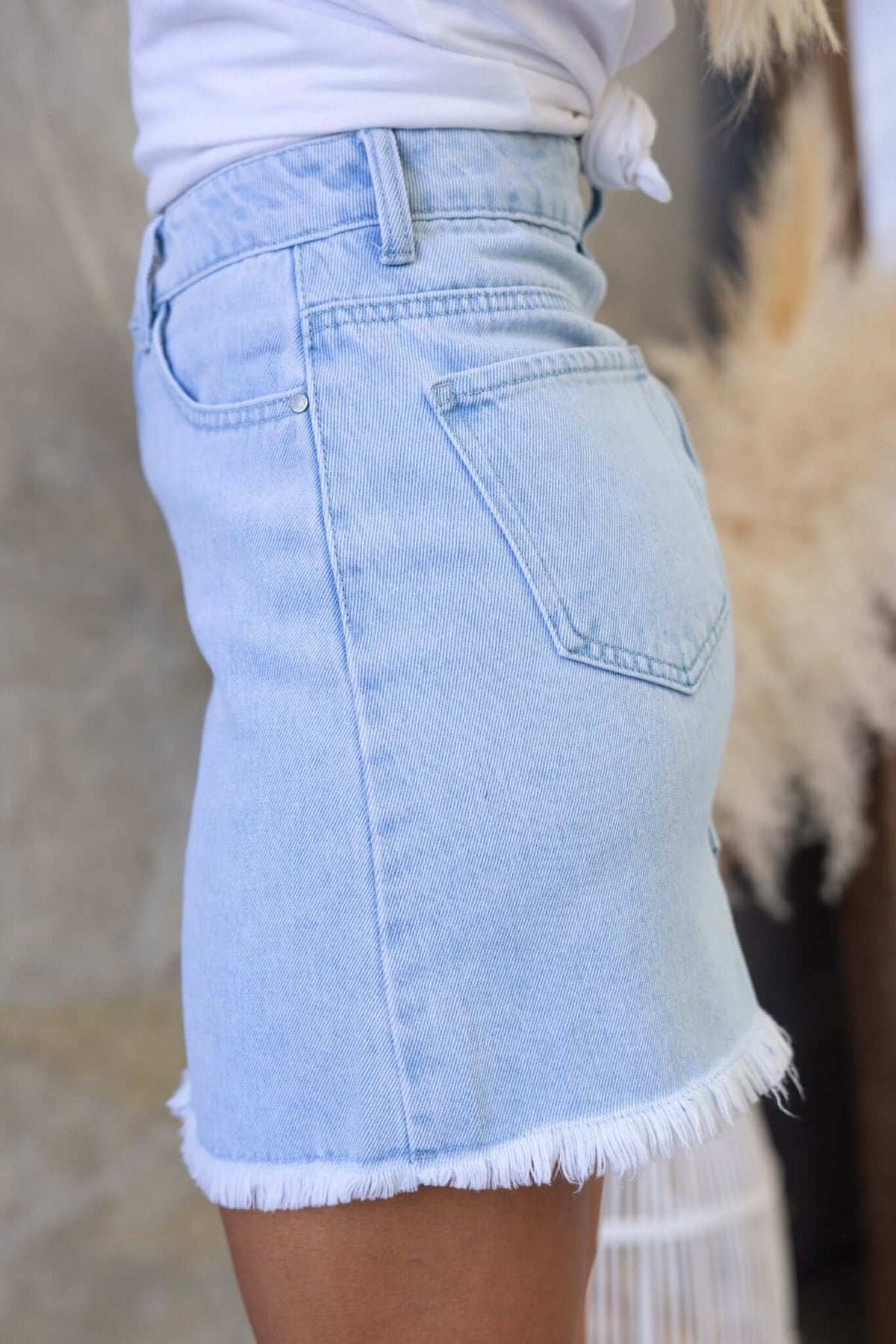 Side view of Orange County Denim Skirt featuring a raw hemline and mid-high waist fit in light denim wash.