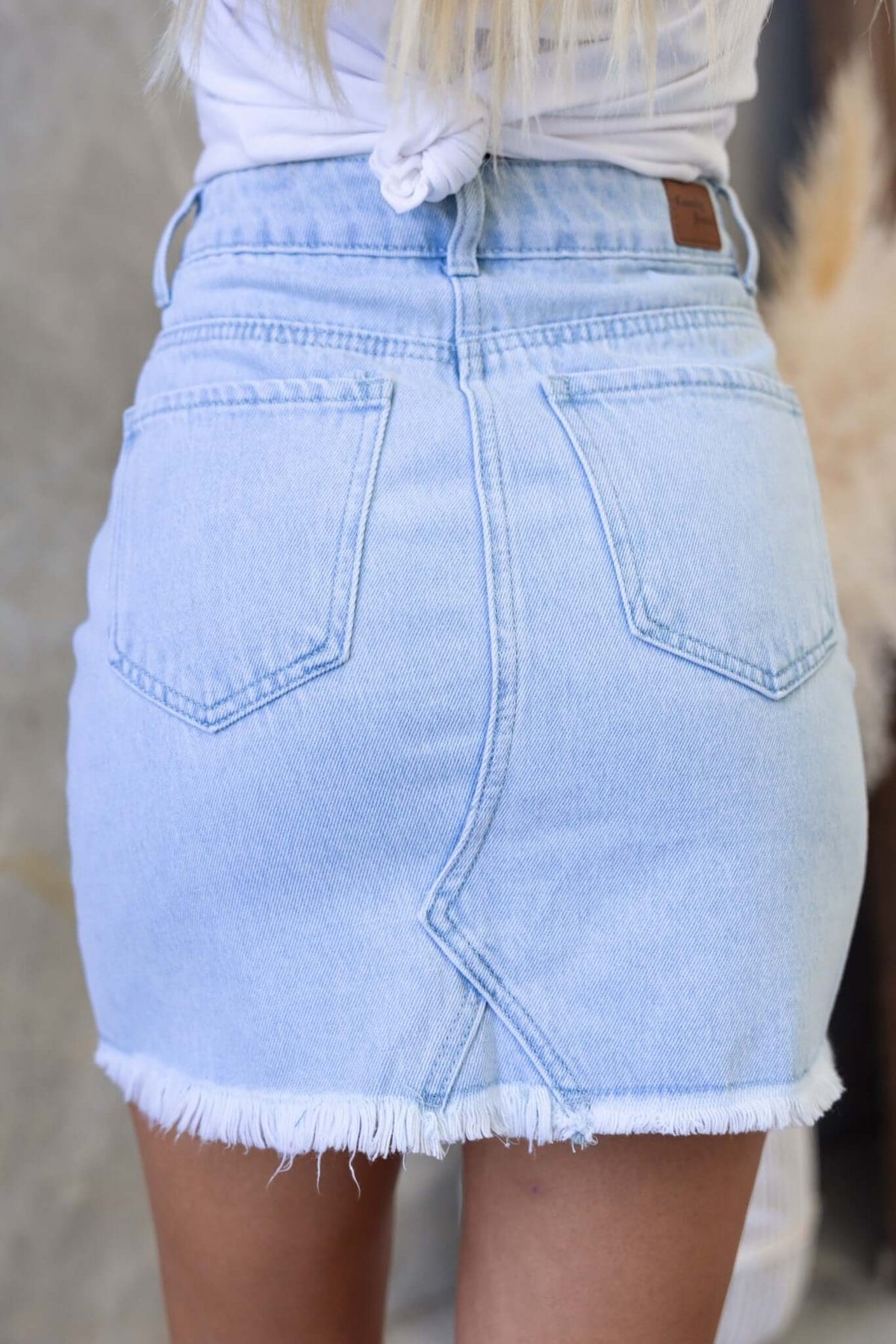 Back view of a light wash orange county denim skirt with raw hemline and pockets, showcasing stylish mid-high waist fit.