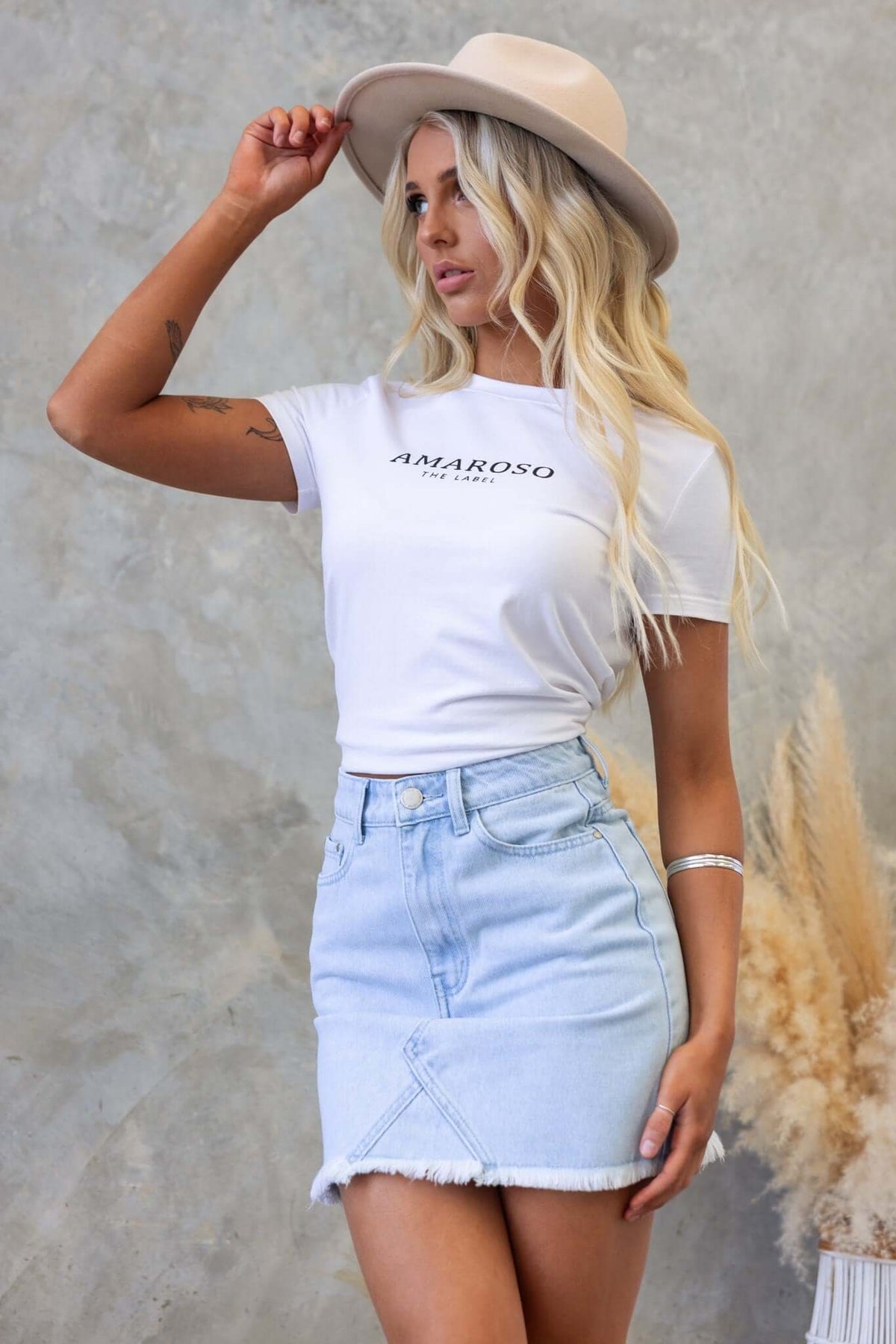 Model wearing Orange County Denim Skirt with mid-high waist and raw hem, styled with a white t-shirt and hat.
