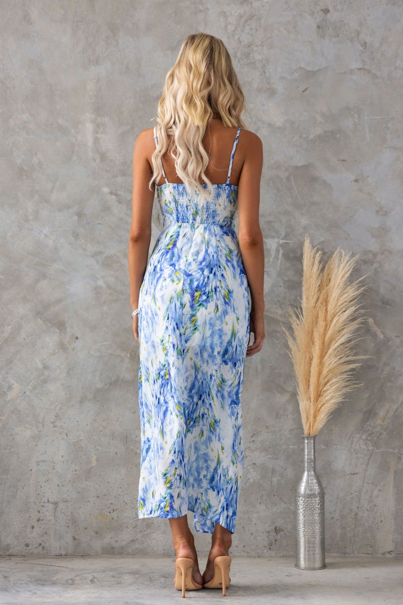 Back view of a woman in a multi-colour maxi dress with adjustable straps and an asymmetric hemline.
