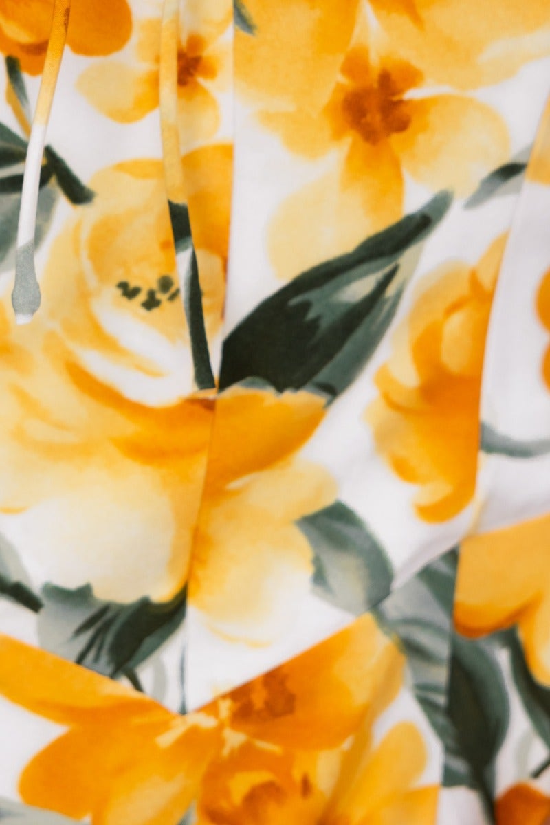 Close-up of floral print with yellow flowers on a white background, showcasing the fabric texture of a maxi dress.