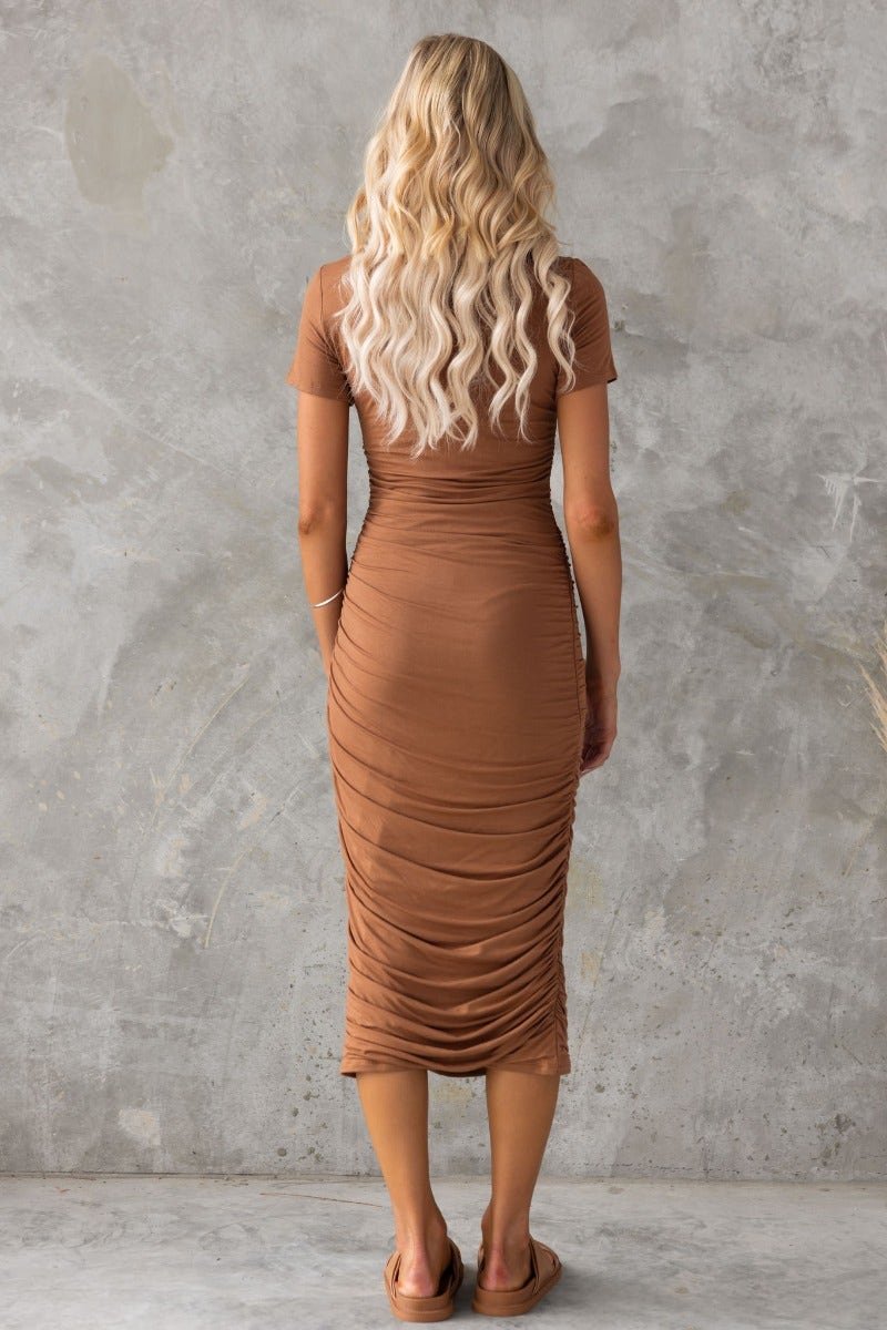 Back view of a woman in a stylish brown bodycon midi dress with side ruching, showcasing a fitted silhouette.