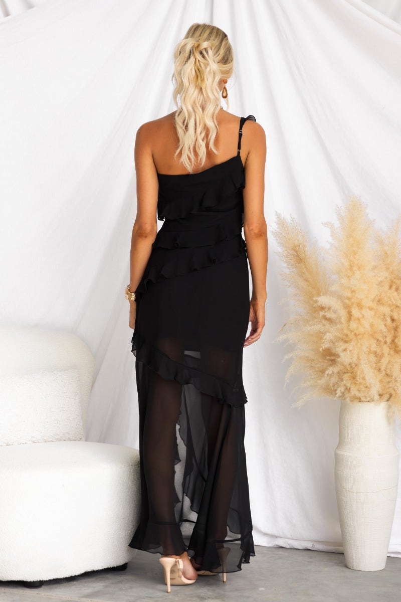 Back view of a black one-shoulder maxi dress with ruffle detail and split, styled for a chic look.
