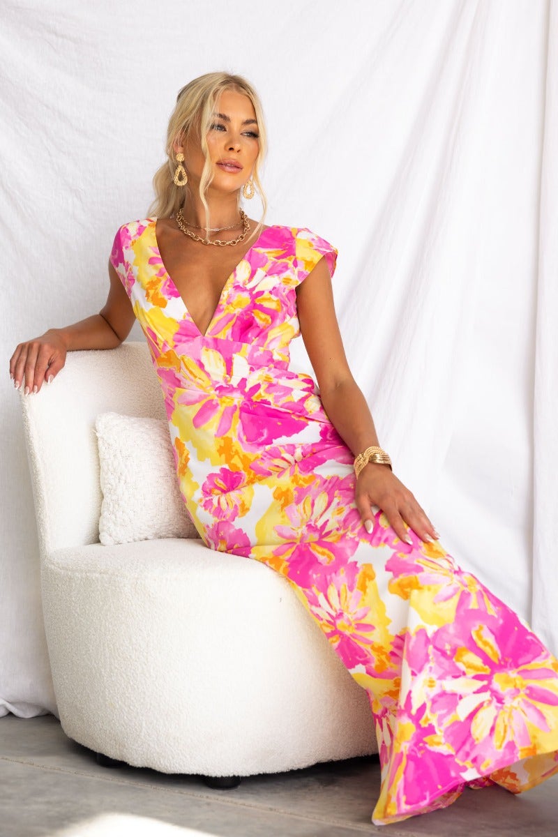 Model in floral print Live In Colour Maxi Dress with V-neckline and cap sleeves, posing elegantly on a white chair.