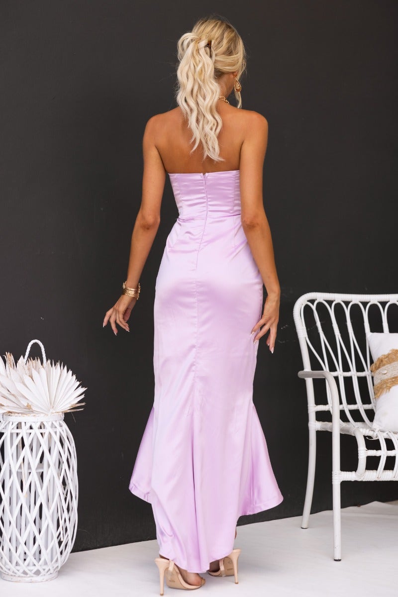 Back view of a model wearing a strapless satin maxi dress in lavender, showcasing a fitted bodice and asymmetric hemline.