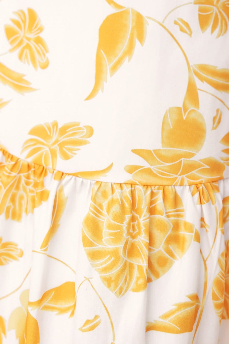 Close-up of floral print in yellow on white fabric, featuring elastic details and a gathered waistline.