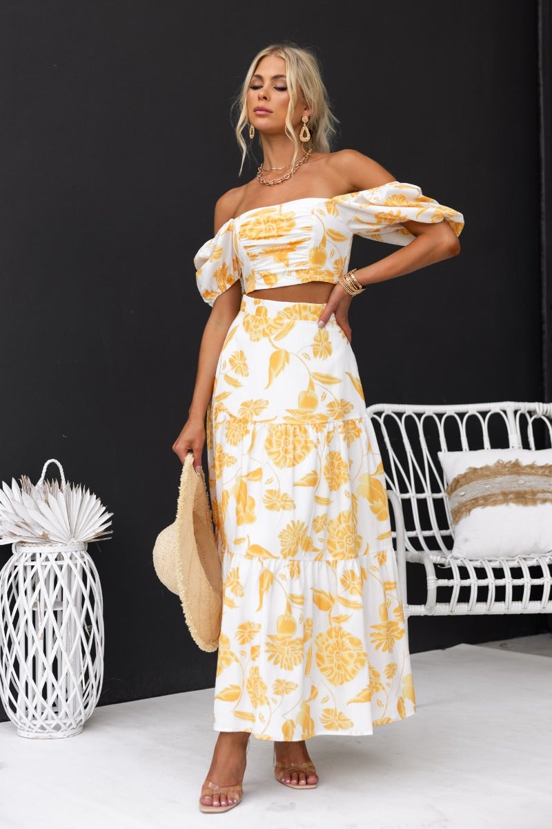 Woman in floral print crop top and maxi skirt set, accessorized with a sun hat and earrings, posing elegantly.