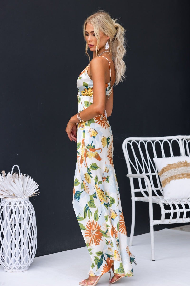 Model wearing a Disappear Maxi Dress with floral print, adjustable straps, and a flowing design, posed against a dark background.