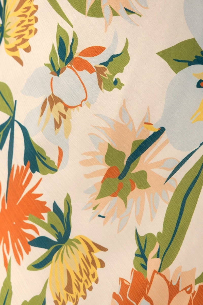 Close-up view of colorful floral pattern featuring vibrant blooms in orange, yellow, and green on a light background.