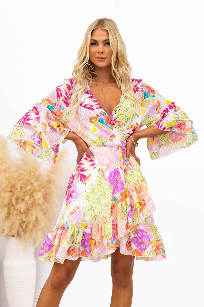 Fools Gold wrap dress featuring vibrant floral patterns, flared sleeves, and a playful ruffled hemline.